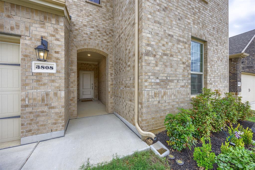 3808 High Country Road Aubrey, TX 76227 - Photo 2 of 36 Arched entryway featuring a recessed ceiling light, brick facade, and a carriage-style exterior light fixture
