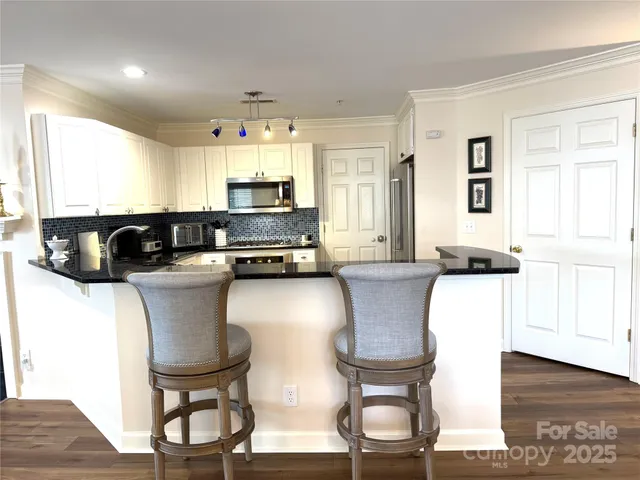 a kitchen with stainless steel appliances granite countertop a stove a sink a microwave a dining table and chairs with wooden floor