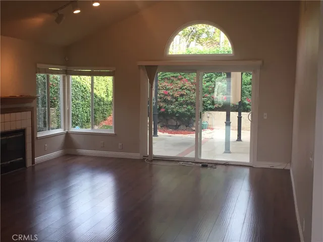 an empty room with wooden floor fireplace and windows