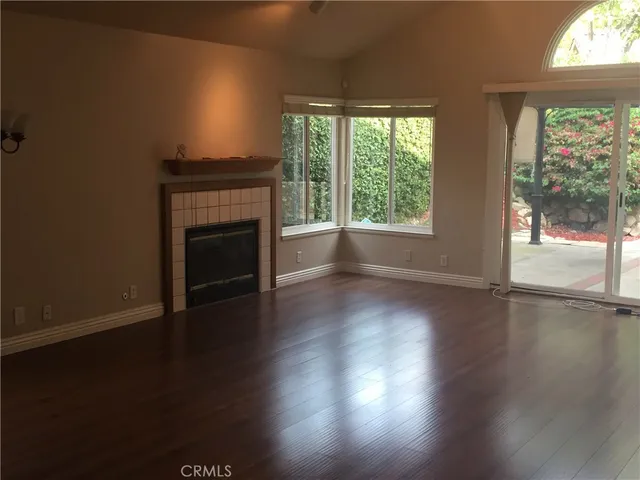 an empty room with wooden floor fireplace and windows