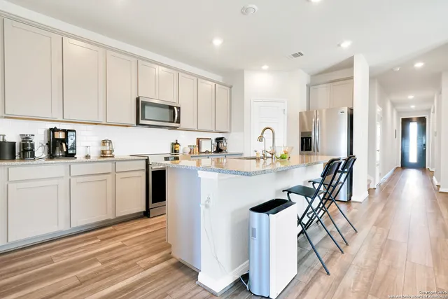 a kitchen with stainless steel appliances granite countertop a refrigerator a stove top oven a sink dishwasher and white cabinets with wooden floor