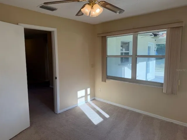 an empty room with a window and chandelier fan