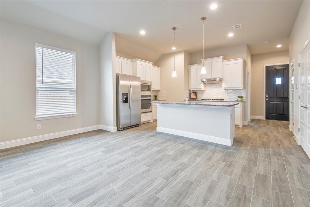 2301 Ruff Road Denton, TX 76205 - Photo 10 of 23 Open concept kitchen featuring an island with a stone countertop, white shaker cabinetry, stainless steel appliances, and wood-look tile flooring