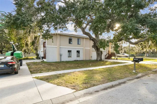a view of a white house next to a yard with a large tree