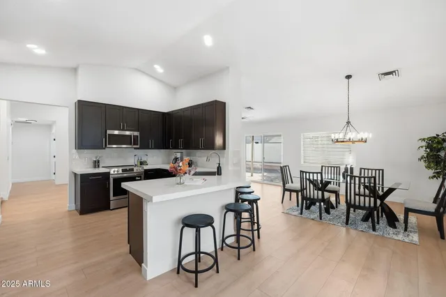 a kitchen with stainless steel appliances granite countertop a stove top oven a sink a dining table and chairs with wooden floor