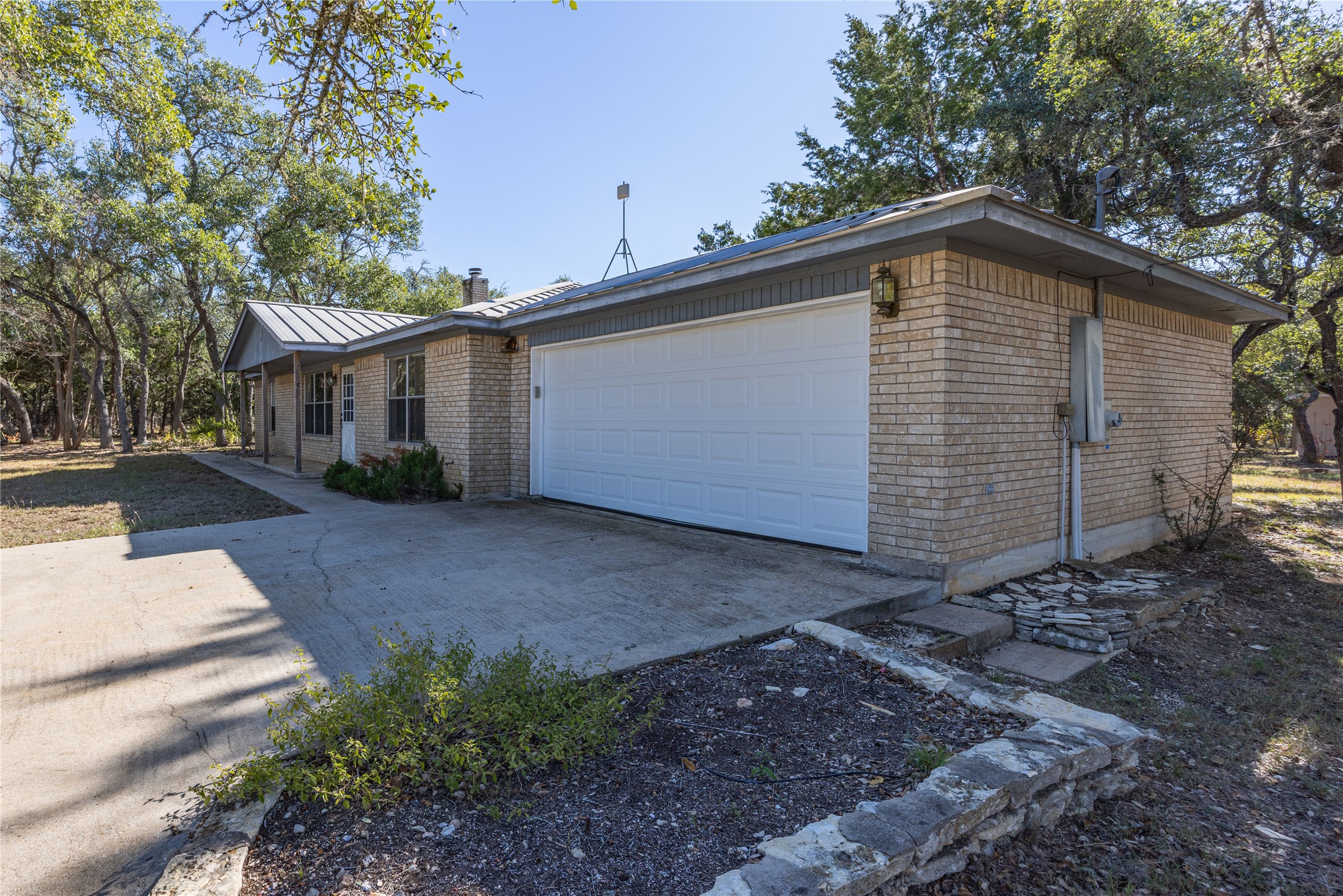 2501 Fischer Store Road Wimberley, TX 78676 - Photo 2 of 23 Brick exterior with a metal roof, featuring an attached two-car garage and a covered front porch