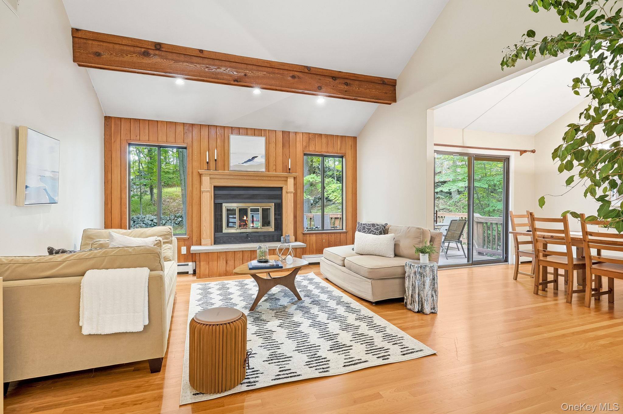 43 Powder Horn Road Cortlandt Manor, NY 10567 - Photo 6 of 35 The living room features a wood-burning fireplace with a stone hearth, oversized windows, and a sliding glass door to the exterior deck