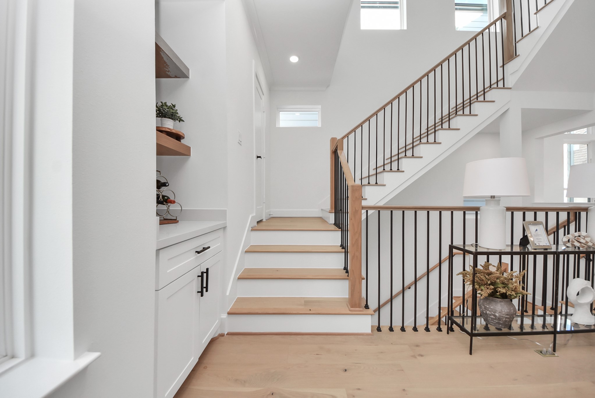 927 Fisher Street, Unit B Houston, TX 77018 - Photo 34 of 47 Ascend this bright, modern staircase with wooden steps and sleek metal railings. A built-in cabinet with open shelving and decorative touches like plants and a lamp create a welcoming and stylish entryway.