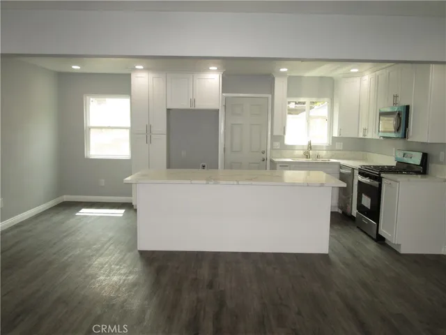 a large white kitchen with kitchen island a sink dishwasher a stove and a dining table with wooden floor