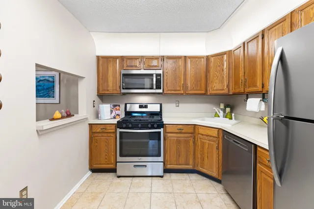 a kitchen with stainless steel appliances granite countertop a stove top oven a sink dishwasher and a refrigerator with wooden cabinets