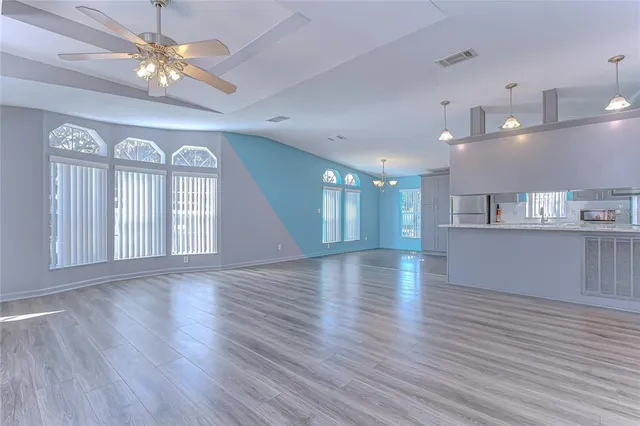 an empty room with wooden floor a chandelier fan and windows