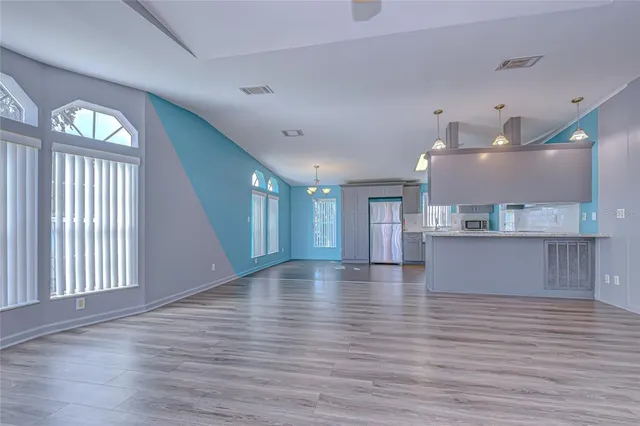 a view of an empty room and kitchen with wooden floor