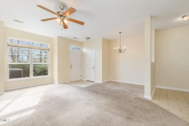 an empty room with chandelier fan and windows