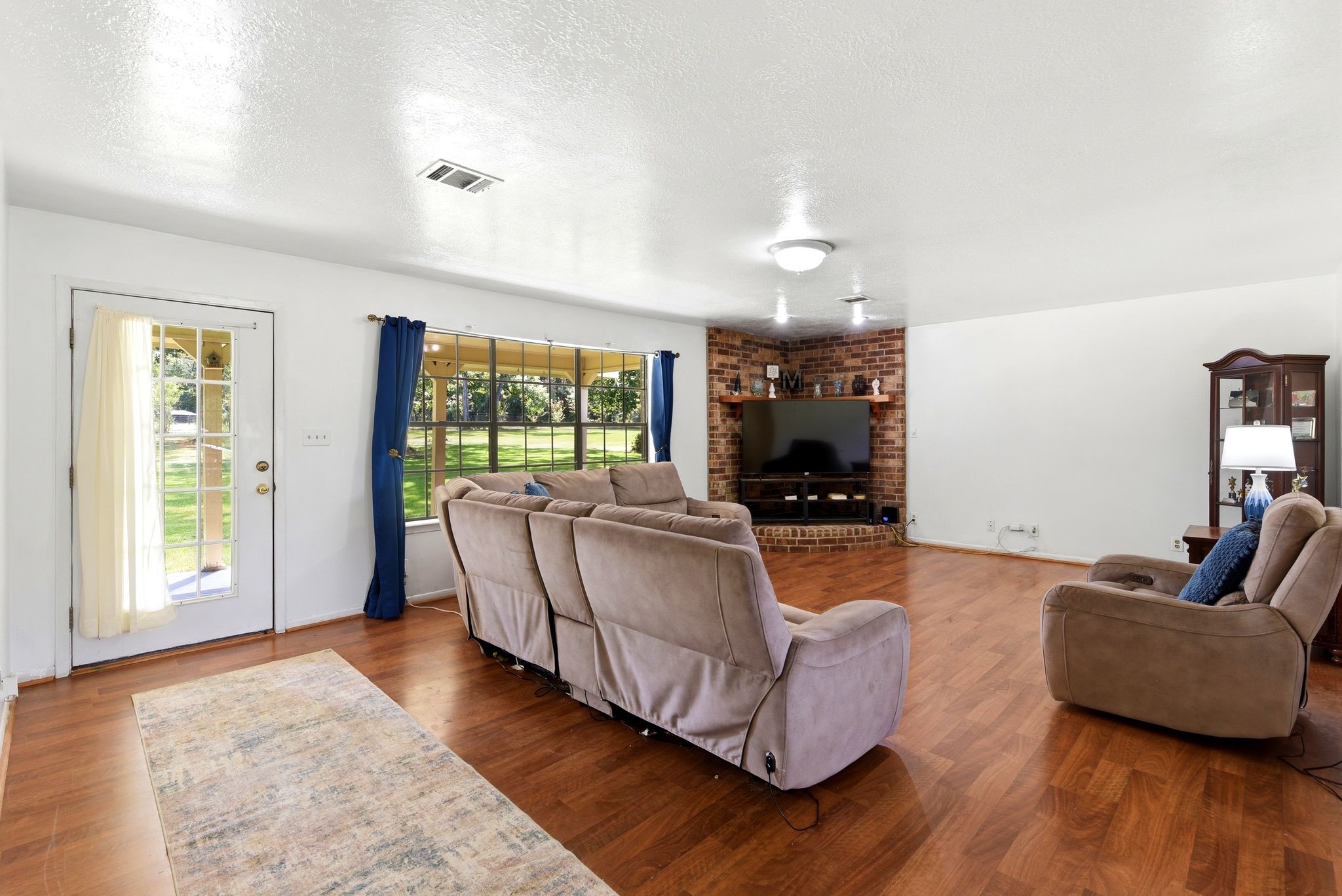 151 Parker Road New Waverly, TX 77358 - Photo 7 of 36 Spacious living room with warm hardwood floors, a cozy brick accent wall, and large windows offering plenty of natural light.
