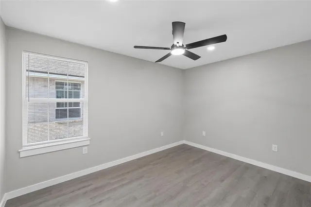 an empty room with wooden floor ceiling fan and window