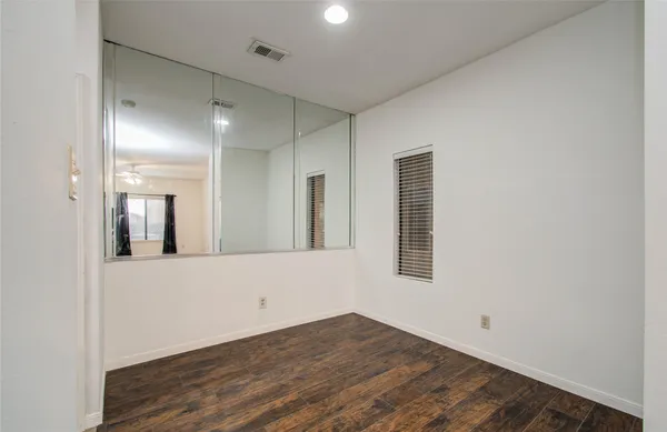 a view of an empty room with wooden floor and a mirror