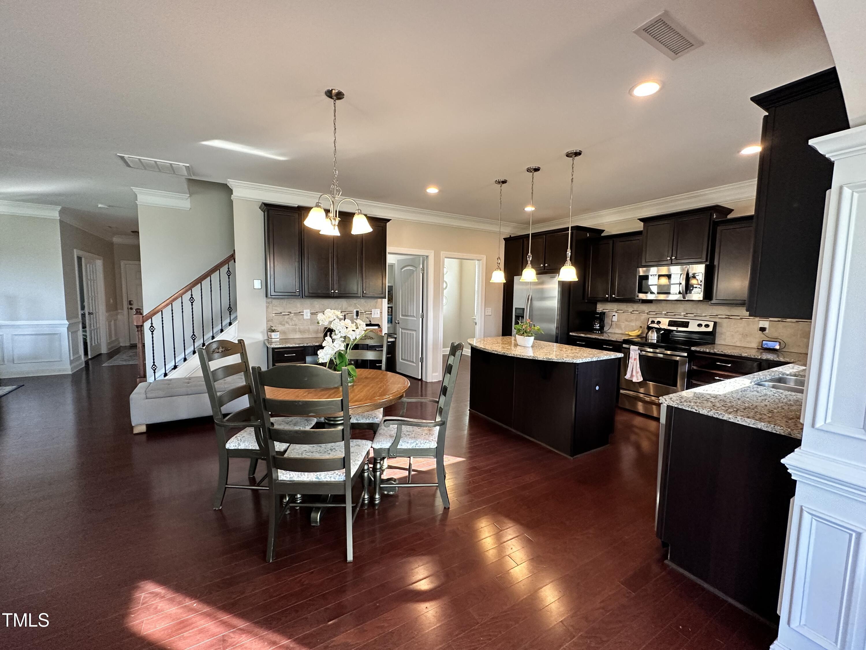 8305 Pin Cherry Drive Willow Spring, NC 27592 - Photo 18 of 60 a kitchen with stainless steel appliances granite countertop a refrigerator a stove top oven a dining table and chairs with wooden floor