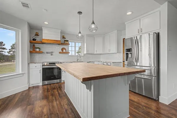 a kitchen with stainless steel appliances granite countertop a refrigerator a sink dishwasher a stove and white countertops with wooden floor