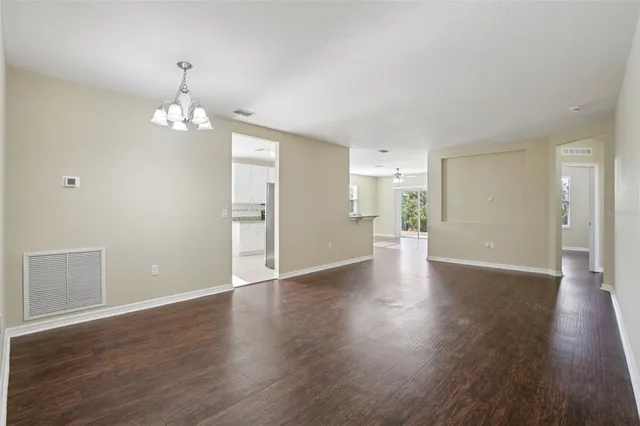 a view of an empty room with wooden floor and kitchen