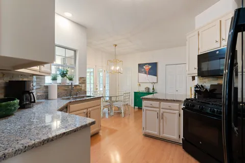 a kitchen with stainless steel appliances granite countertop a stove a sink and white cabinets with wooden floor