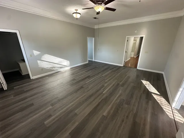 a view of an empty room with wooden floor and a ceiling fan