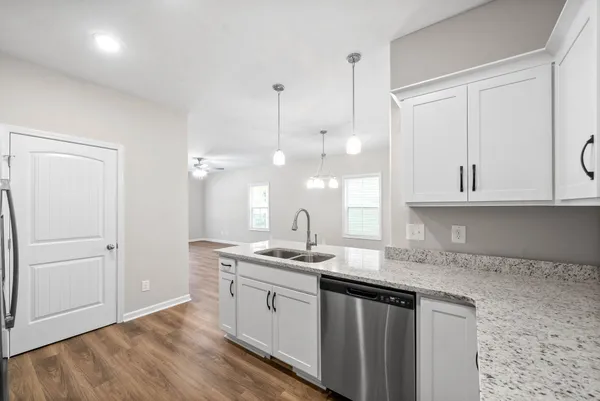a kitchen with a sink dishwasher and white cabinets with wooden floor