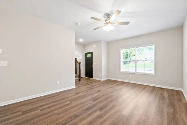 an empty room with wooden floor chandelier fan and windows