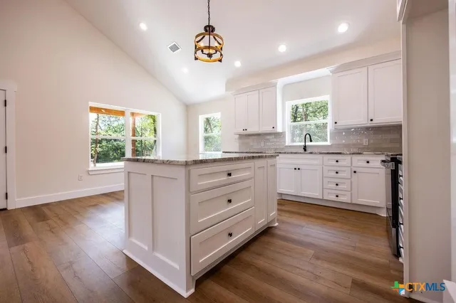 a kitchen with stainless steel appliances granite countertop a stove a sink and white cabinets with wooden floor next to windows