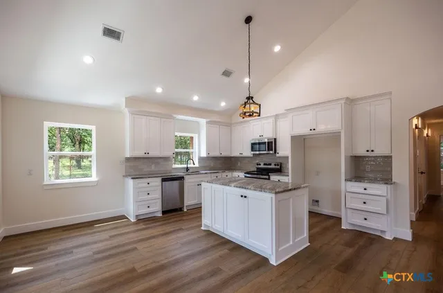 a kitchen with stainless steel appliances kitchen island granite countertop a stove a refrigerator a sink a oven and a dining table with wooden floor