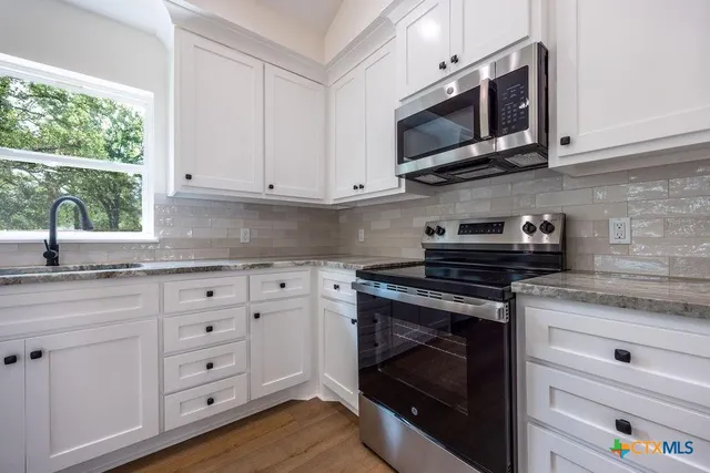 a kitchen with granite countertop white cabinets stainless steel appliances and a sink