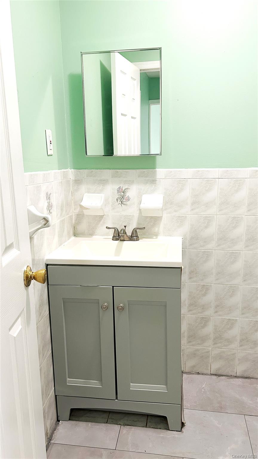 93-26 197th Street, Unit # 3 Queens, NY 11423 - Photo 11 of 14 Bathroom featuring tile walls, wainscoting, vanity, and light tile patterned flooring