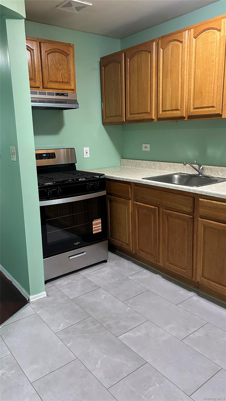 93-26 197th Street, Unit # 3 Queens, NY 11423 - Photo 14 of 14 Kitchen with stainless steel range with gas stovetop, brown cabinets, light countertops, and under cabinet range hood