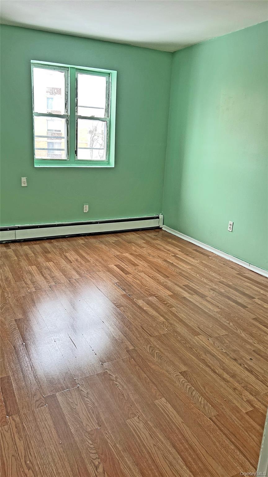 93-26 197th Street, Unit # 3 Queens, NY 11423 - Photo 10 of 14 Empty room featuring a baseboard heating unit and wood-type flooring