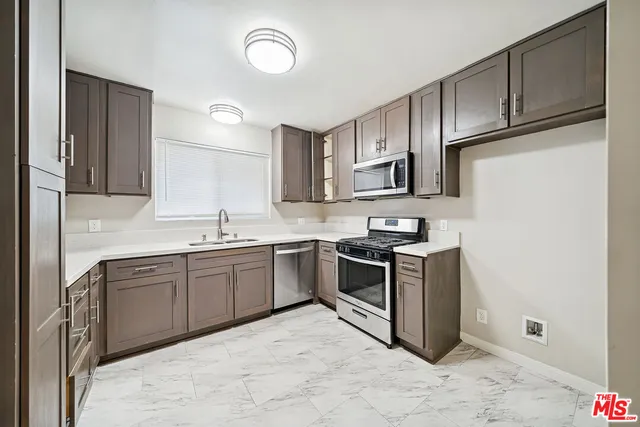 a kitchen with stainless steel appliances granite countertop a stove top oven a sink dishwasher and a refrigerator with wooden cabinets