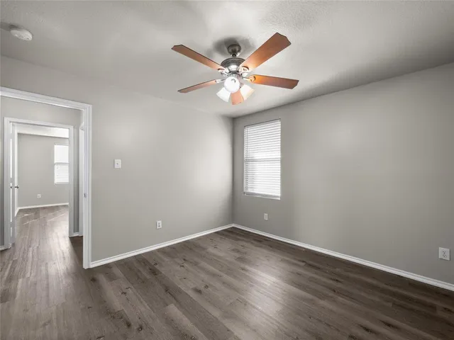 a view of an empty room with wooden floor and a ceiling fan