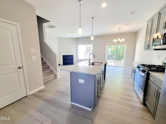 a kitchen with stainless steel appliances granite countertop a refrigerator a sink dishwasher a stove and a dining table with wooden floor