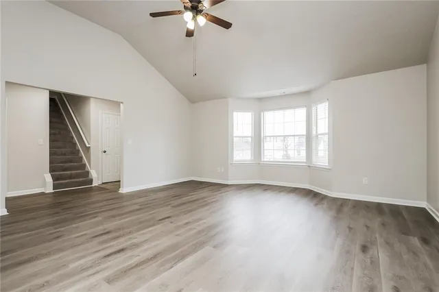 an empty room with wooden floor fan and windows