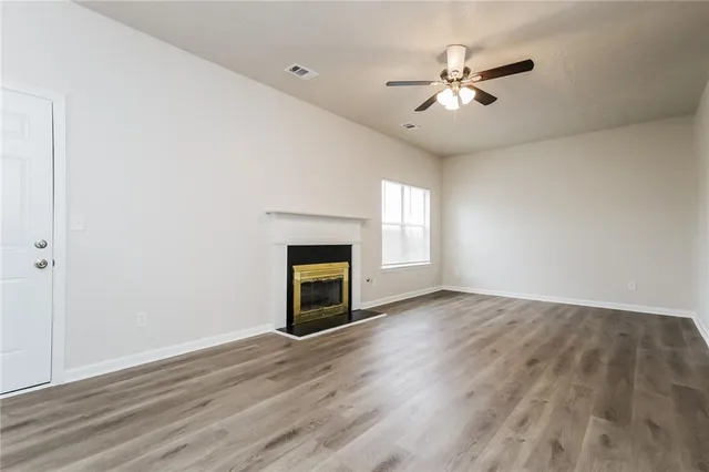 an empty room with wooden floor fan and windows
