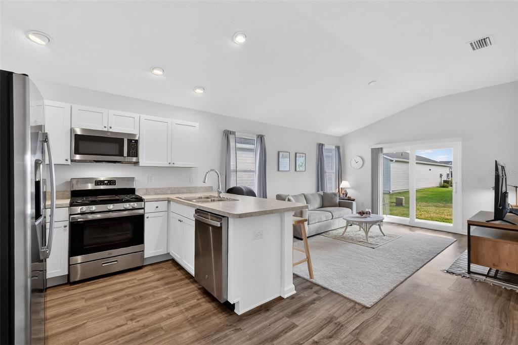 832 Conroe Street The Villages, FL 34762 - Photo 8 of 37 a open kitchen with stainless steel appliances granite countertop a stove top oven a sink dishwasher a dining table and chairs with wooden floor