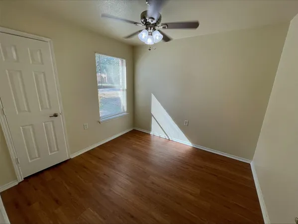 an empty room with wooden floor chandelier fan and windows