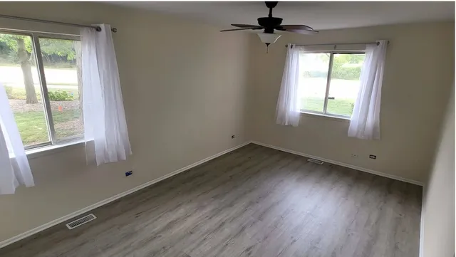 an empty room with wooden floor fan and windows