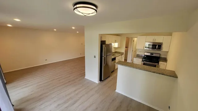 an empty room with wooden floor a kitchen view and windows