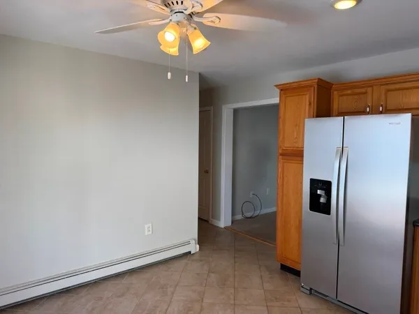 a view of a refrigerator in kitchen and an empty room with wooden floor