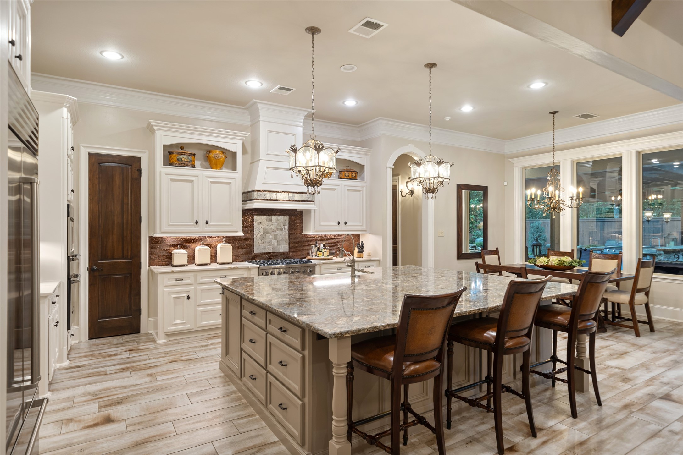 59 East Ambassador Bend Spring, TX 77382 - Photo 10 of 48 This spacious, elegantly designed kitchen features a sprawling Cambria quartz island and custom white cabinetry. The warm wood accents and rich glass tile backsplash add depth and character, while the stylish pendant lighting creates a welcoming ambiance. The open-concept layout flows seamlessly into the bright breakfast area with expansive windows, making it perfect for both everyday living and entertaining.