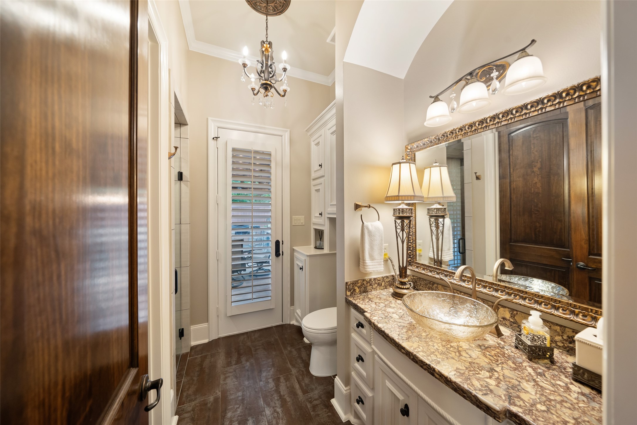 59 East Ambassador Bend Spring, TX 77382 - Photo 21 of 48 This beautifully designed secondary bathroom offers convenient access from the backyard, making it perfect for poolside use. Featuring built-in storage for added functionality, the space is elevated by elegant chandeliers and sleek quartz countertops. A striking glass vessel sink serves as a unique focal point, adding a modern, spa-like touch.