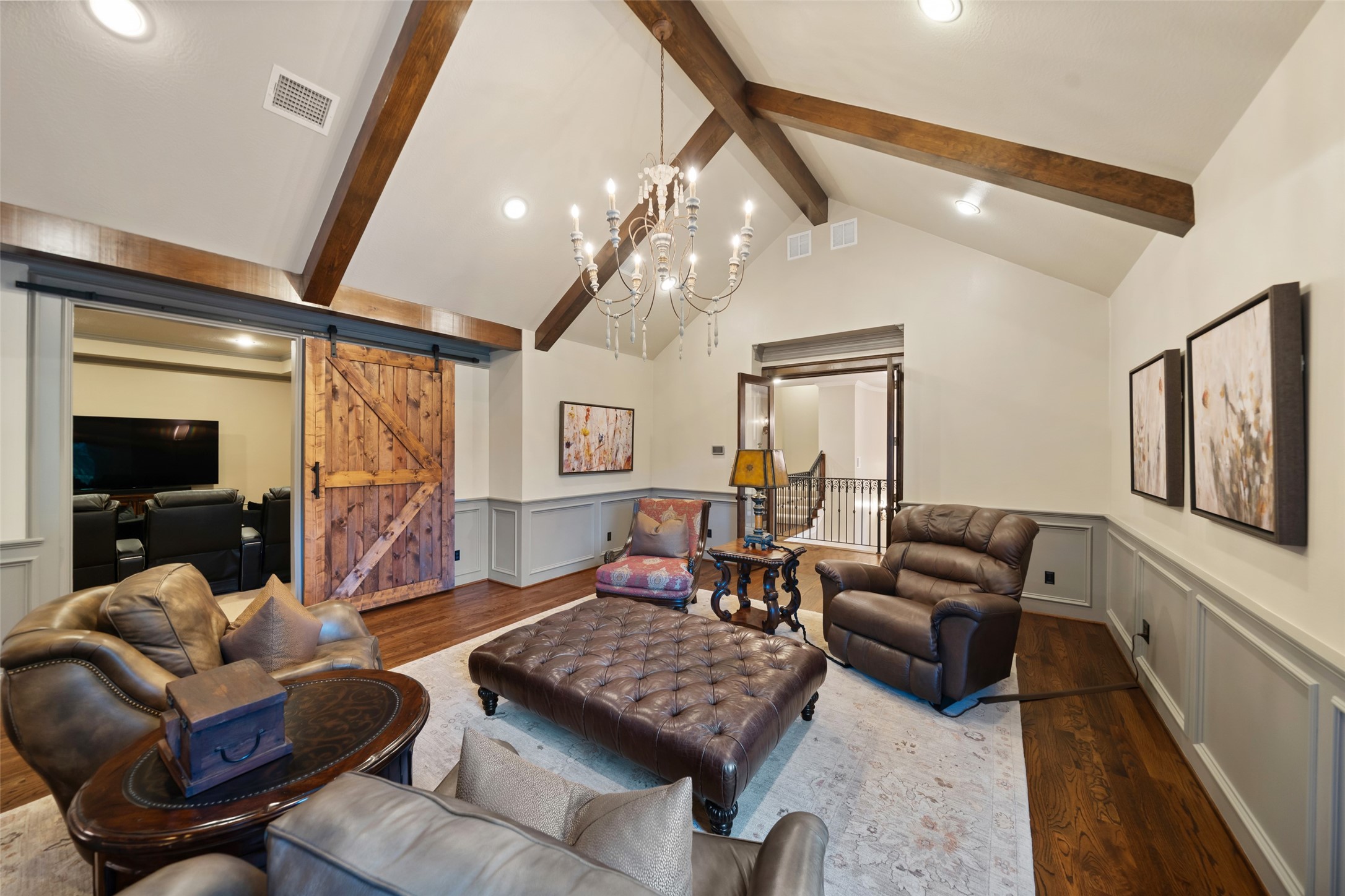 59 East Ambassador Bend Spring, TX 77382 - Photo 25 of 48 This warm and inviting upstairs living space features a vaulted ceiling with handsome wood beams and a central chandelier that enhances the room’s sense of openness. Rich hardwood flooring runs throughout, complemented by neutral walls with detailed wainscoting for added character. The sliding barn-style door adds both functionality and architectural interest, providing access to the adjacent media room.
