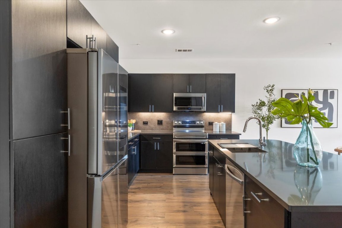 4801 Springdale Road, Unit 1107 Austin, TX 78723 - Photo 8 of 40 Kitchen featuring stainless steel appliances, light wood finished floors, dark stone countertops, a kitchen island with sink, and modern cabinets