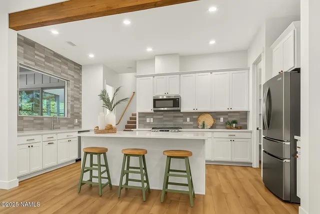 a kitchen with stainless steel appliances granite countertop a refrigerator a sink dishwasher a stove and white cabinets with wooden floor