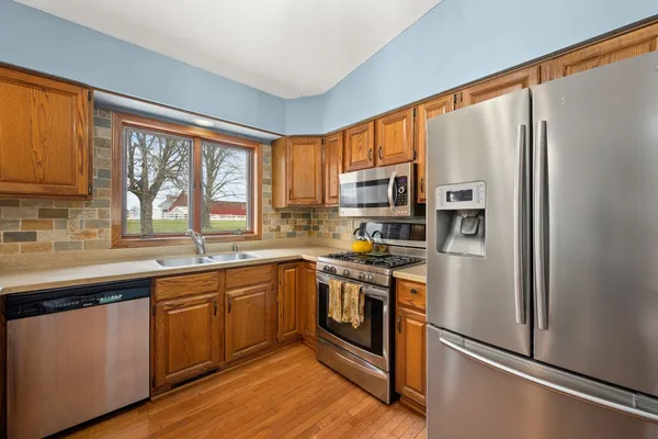 a kitchen with stainless steel appliances granite countertop a refrigerator a sink dishwasher a stove top oven a refrigerator with wooden floor and cabinets