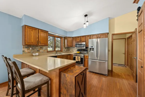 a kitchen with stainless steel appliances granite countertop a refrigerator a sink dishwasher a stove and a dining table with wooden floor